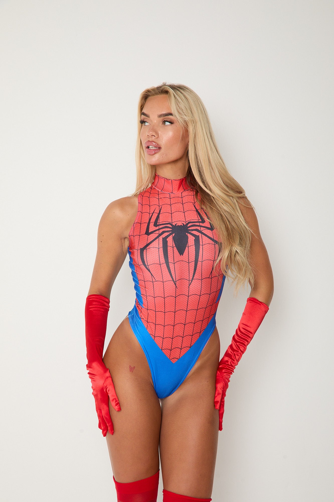 Woman wearing SPIDERWOMAN bodysuit with red gloves and stockings, embodying a bold and fearless superhero look.