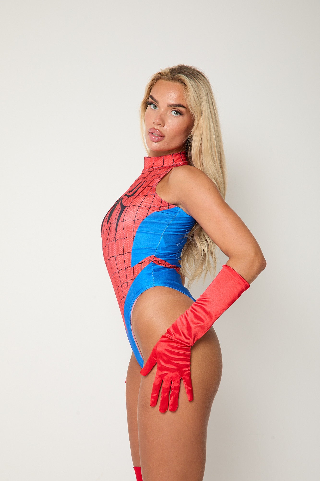 Woman wearing SPIDERWOMAN bodysuit with red gloves and red stockings, striking a confident pose against a plain background.