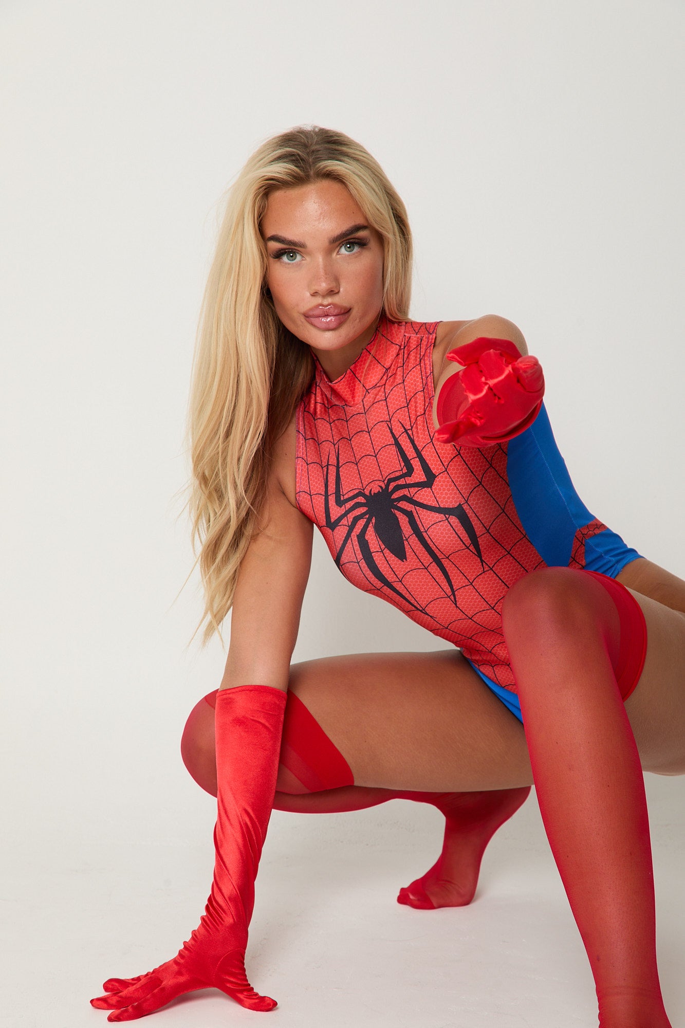 Woman wearing Spiderwoman bodysuit with red stockings and gloves, posing confidently in superhero costume for Halloween or cosplay.