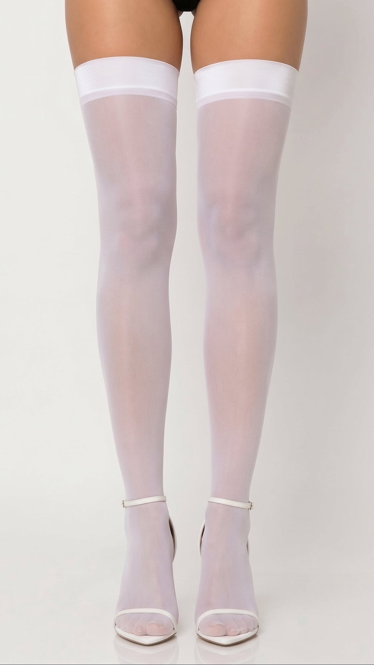 White thigh-high stockings worn by a model, paired with clear high-heeled sandals, shown against a plain light gray studio background.